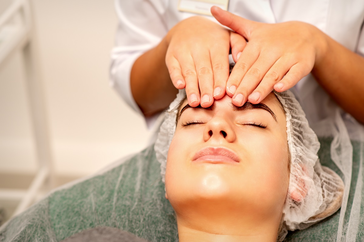 Head massage. Beautiful caucasian young white woman receiving a head and forehead massage with closed eyes in a spa salon.